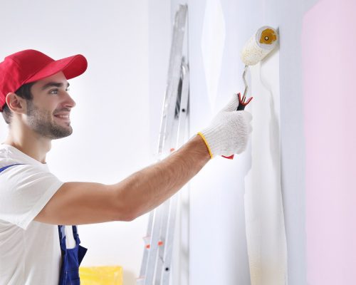 Young worker painting wall in room